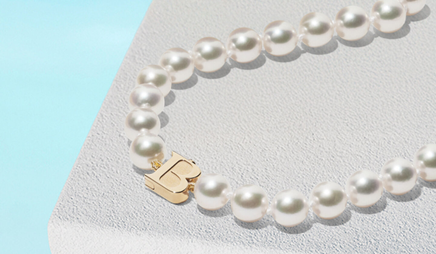 Birks Pearls gold strand necklace on a blue background.